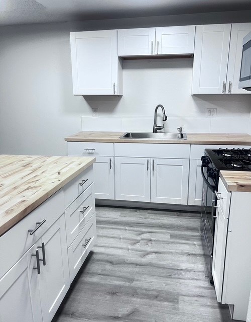 A kitchen with white cabinets and a wooden counter top.